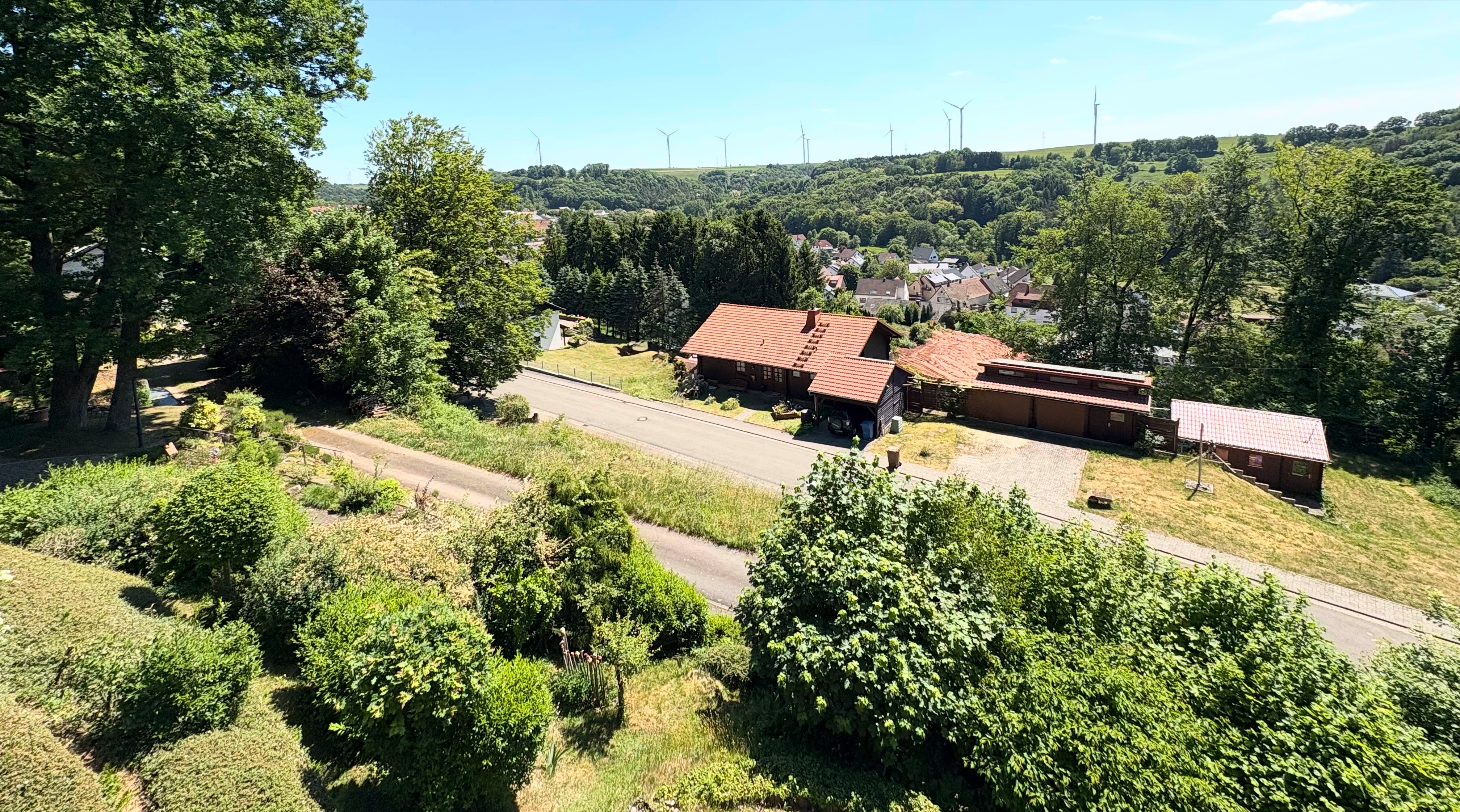 Ausblick auf Lambsborn. Es sind überwiegend Bäume und Grünflächen zu sehen, sowie eine verkehrsberuhigte Straße.